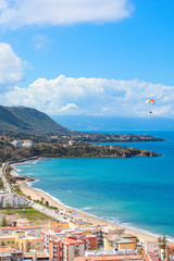 Naklejka premium Paraglider flying over the amazing sea landscape by coastal Cefalu in Italian Sicily. Captured on a vertical photography with hills behind the beautiful bay