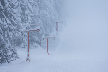 Frozen ski lift covered with snow. Hard winter conditions, snowfall and fog.