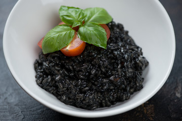 Close-up of a white bowl with squid-ink risotto, selective focus, studio shot
