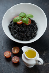 Fototapeta na wymiar Risotto with squid-ink, cherry tomatoes, fresh green basil and olive oil, vertical shot on a dark brown stone background