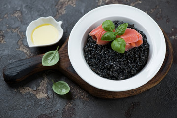 Fototapeta na wymiar Plate of risotto with squid-ink and salmon fillet, studio shot on a brown stone background