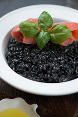 Fototapeta na wymiar Close-up of squid-ink risotto served with salmon fillet and green basil in a white plate