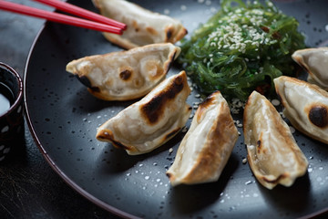 Fried gyoza dumplings served with seaweed salad on a black plate, closeup, selective focus