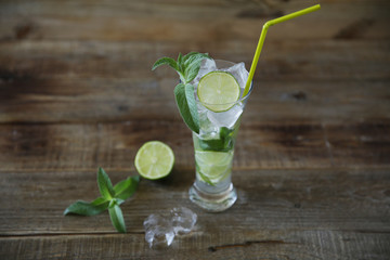 Mojito cocktail in glass with ice, mint and green lime on a wooden rustic background with copy space for text.