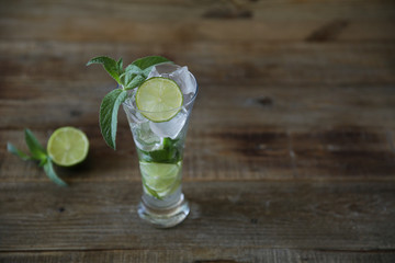 Mojito cocktail in glass with ice, mint and green lime on a wooden rustic background with copy space for text.