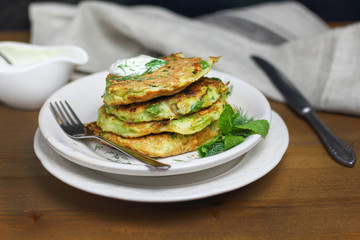 Proper nutrition, vegetarian breakfast gluten free,zucchini courgette pancakes with beans, mint on white plates with sour greek yogurt, black background, towel, fork, knife on wooden surface