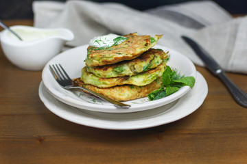 Proper nutrition, vegetarian breakfast gluten free,zucchini courgette pancakes with beans, mint on white plates with sour greek yogurt, black background, towel, fork, knife on wooden surface