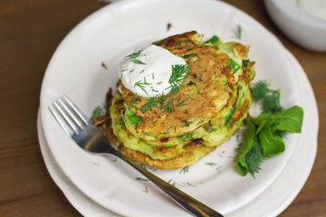 Proper nutrition, vegetarian breakfast gluten free,zucchini courgette pancakes with beans, mint on white plates with sour greek yogurt, black background, towel, fork, knife on wooden surface
