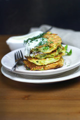 Proper nutrition, vegetarian breakfast gluten free,zucchini courgette pancakes with beans, mint on white plates with sour greek yogurt, black background, towel, fork, knife on wooden surface