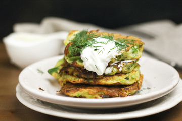 Proper nutrition, vegetarian breakfast gluten free,zucchini courgette pancakes with beans, mint on white plates with sour greek yogurt, black background, towel, fork, knife on wooden surface