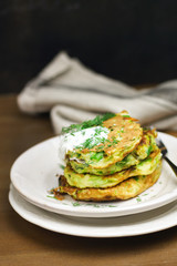 Proper nutrition, vegetarian breakfast gluten free,zucchini courgette pancakes with beans, mint on white plates with sour greek yogurt, black background, towel, fork, knife on wooden surface