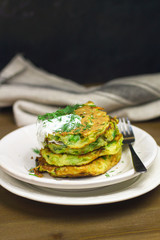 Proper nutrition, vegetarian breakfast gluten free,zucchini courgette pancakes with beans, mint on white plates with sour greek yogurt, black background, towel, fork, knife on wooden surface