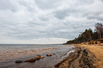 lonely empty sea beach with white sand, large rocks and old wooden trunks on the shore