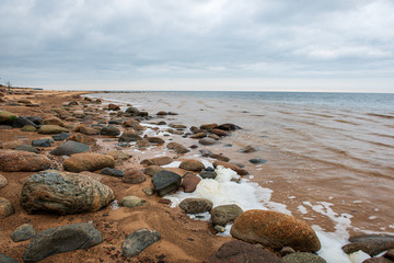 lonely empty sea beach with white sand, large rocks and old wooden trunks on the shore