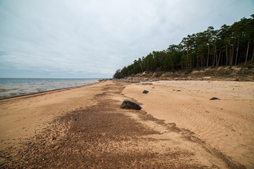 lonely empty sea beach with white sand, large rocks and old wooden trunks on the shore