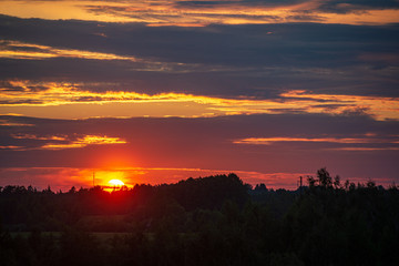 dramatic red sunset colors in the sky above trees and fields