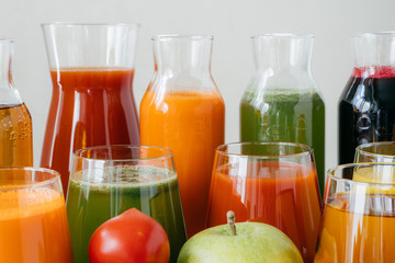 Close up shot of glass bottles filled with colorful juice made of various vegetables and fruit, red tomato and green apple in foreground. Fresh detox drink