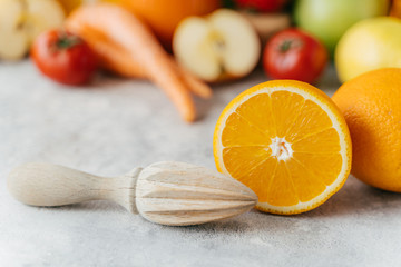 Sliced orange and wooden squeezer against blurred fruit and vegetables background. Squeezing of fresh citrus fruit. Healthy nutrition concept