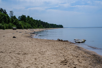 lonely empty sea beach with white sand, large rocks and old wooden trunks on the shore