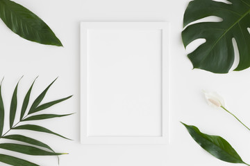 Top view of a white frame mockup with tropical leaves decoration. Portrait orientation.