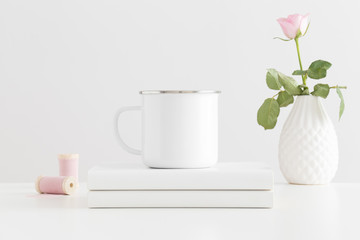 Enamel mug mockup with a pink rose and books on a white table.