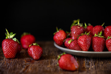 Strawberries scattered and in a plate on a wooden background.