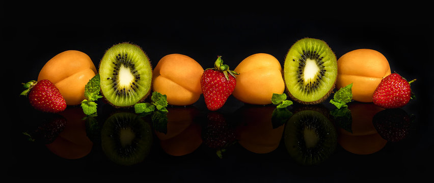 Fruit platter of apricots, kiwi, strawberries and mint, on a transparent dark background with reflection.