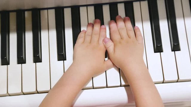 Closeup top view of cute small hands of caucasian baby isolated at keyboard of piano. Child trying to play music.