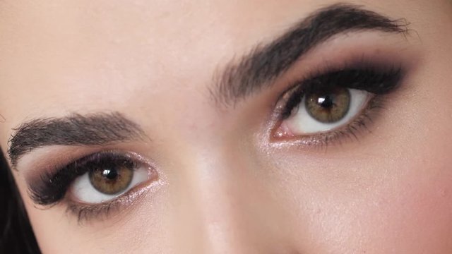 Detail closeup shot of young beautiful brown haired woman green eyes with gorgeous trendy professional makeup, beautiful long eyelashes, perfect eyebrows, demonstrates artist portfolio emotionally