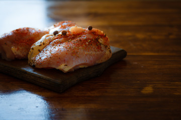 On a wooden brown table lies a set of vegetables and a fresh, skinless breast for cooking.