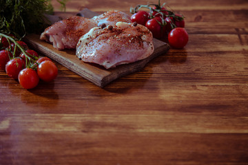On a wooden brown table lies a set of vegetables and a fresh, skinless breast for cooking.