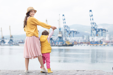 Happy family, mother, child at the Marina. The mother holds the child's hands and smiling on the background of the sea and  port. The concept of happy parents and children together, healthy lifestyle