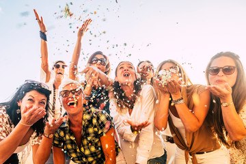 People having fun in party celebration friends concept - group of young and adult women all together laughing blowing coloured confetti - friendship and love for lifestyle with mixed active generation