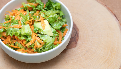 Vegetable salad with avocado, carrot, greens on wooden background