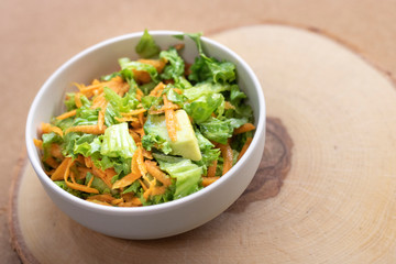 Vegetable salad with avocado, carrot, greens on wooden background