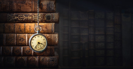 Vintage clock hanging on a chain on the background of old books. Old watch as a symbol of passing time. Concept on the theme of history, nostalgia, old age. Retro style. - obrazy, fototapety, plakaty