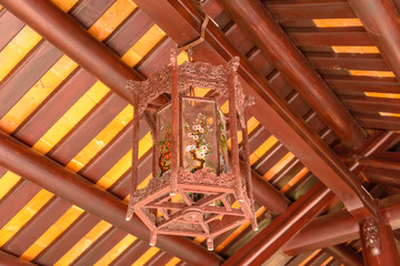 An ornate painted glass lantern hangs from a wooden ceiling in Điện Cần Chánh (Can Chanh Palace) Hoàng thành (Imperial City) a walled citadel built in 1804 in Hue, Vietnam.