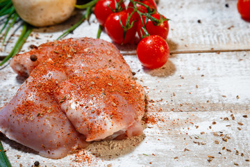 On a wooden brown table lies a set of vegetables and a fresh, skinless breast for cooking.