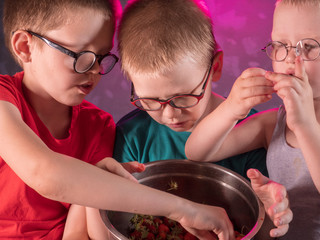 Funny little baby boys blond eating ripe strawberries from large pot. Kids helped to harvest with mom in garden and now enjoys. Children eat healthy organic foods, fresh berries