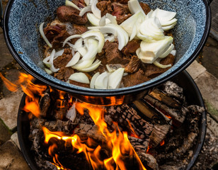 White onions and roasted pieces of beef hang in a pot over an open wood fire for the preparation of...