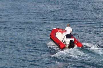 Obraz premium The marina staf is sailing on a red inflatable motorboat to a sailing cruise yacht entering the marina. Pilot assistance with the mooring of a charter boat. Verification of the vessel by the guard