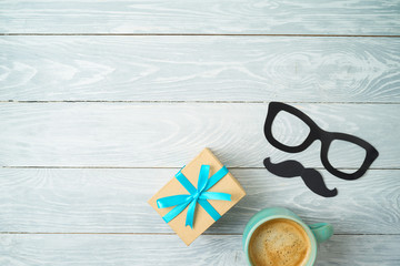 Happy Father's day concept with mustache, coffee cup and gift box over wooden background.