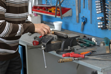 Handyman handles part in cast-iron vice in repair shop