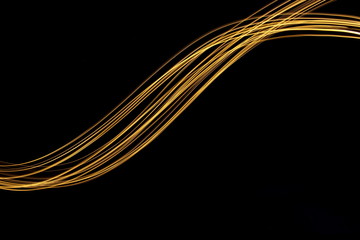 Long exposure, light painting photography.  Vibrant streaks of metallic gold colour against a black...