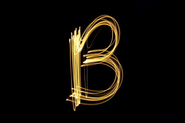 Long exposure, light painting photography.  Single letter B in a vibrant neon metallic yellow gold colour against a black background.  Alphabet series.