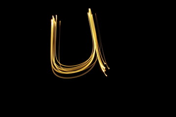 Long exposure, light painting photography.  Single letter U in a vibrant neon metallic yellow gold colour against a black background.  Alphabet series.