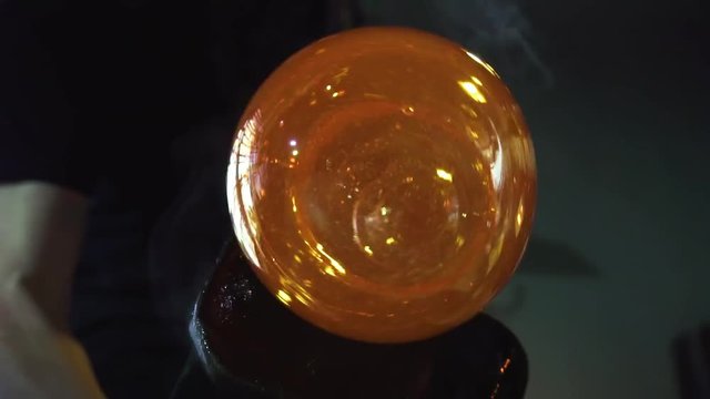 Glassblower in his workshop taking out rod with liquid glass and turning it. Close-up.