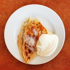 Pancake with sugar and cream on a white plate.