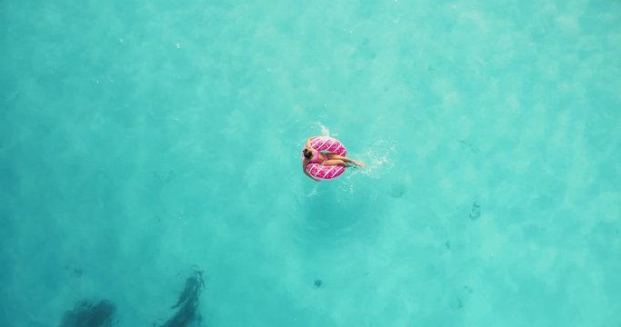 Aerial view of a young woman swimming with the donut swim ring in clear blue sea at sunset in summer. Tropical aerial landscape with slim girl, azure water. Top view from flying drone in slow motion