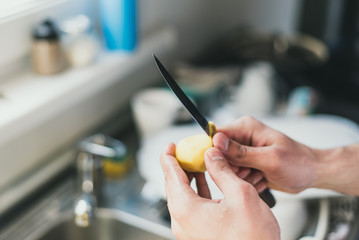 man cleans potatoes with a knife at the sink at home. peel small potatoes. cleaning in the sink.